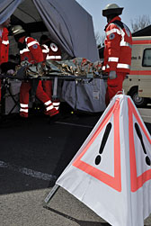 Foto: Ein Warndreieck steht vor dem Patientenzelt, in das Helfer gerade eine Person auf einer Trage transportieren.