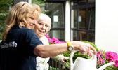 Foto: Pflegekraft gießt mit Seniorin Blumen.